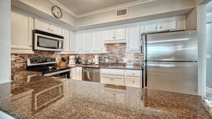 A kitchen with white cabinets, a stainless steel refrigerator, a microwave, a stove, and a coffee maker.