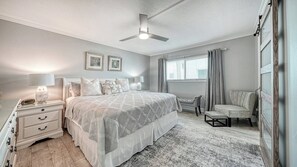 Ein Schlafzimmer mit einem Bett, Nachttischen, einem Schreibtisch, einem Sessel, einem Deckenventilator und einem Fenster mit Vorhängen.
