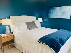 Ein Schlafzimmer mit einem Bett, einem Nachttisch, einer Lampe und einem Bild an der Wand.