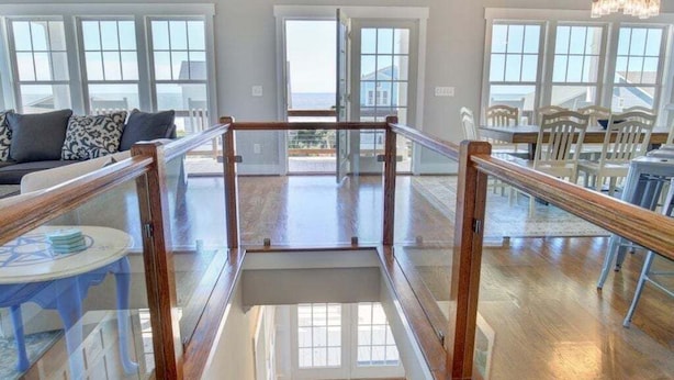 Un intérieur spacieux agrémenté d’un escalier en bois, de rampes en verre et de grandes fenêtres offrant une vue imprenable.