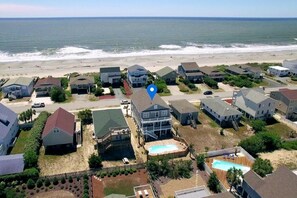 A coastal residential area with houses, a swimming pool, and a beach in the background.