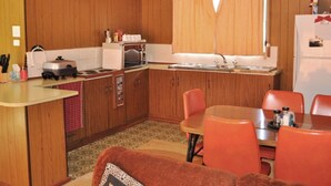 A compact kitchen with wooden cabinets, a microwave, a stove, and a sink. There is a dining table with four chairs and a small rug.