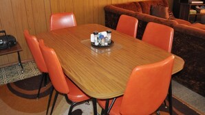 A dining area with a wooden table and orange chairs, a small side table with a radio, and a brown sofa against the wall.