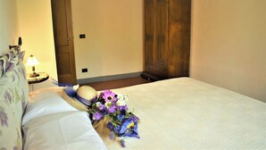 A bedroom with a bed, a wooden wardrobe, a nightstand with a lamp, and a floral bedspread. - Agriturismo Luggiano Apartment "AIA" (Vinci)