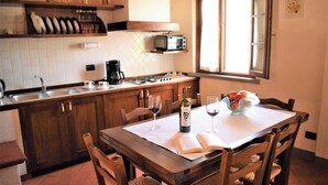 A kitchen with wooden cabinets, a white countertop, a stove, a microwave, and a window with blinds. - Agriturismo Luggiano Apartment "AIA" (Vinci)