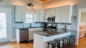 Une cuisine avec des meubles blancs, un îlot central doté de tabourets, un four à micro-ondes et une cuisinière.