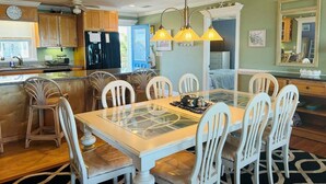 Un coin repas avec une table à plateau en verre, des chaises blanches et un lustre.