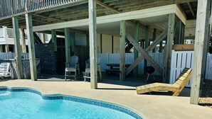 Une piscine avec une terrasse en bois, des chaises longues et un espace patio couvert.