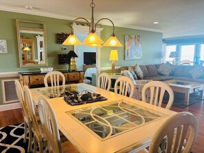 A dining area with a glass-top table, white chairs, and pendant lighting.