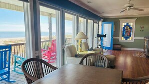 Une pièce avec une table en bois, des chaises, un télescope et une vue sur la plage.