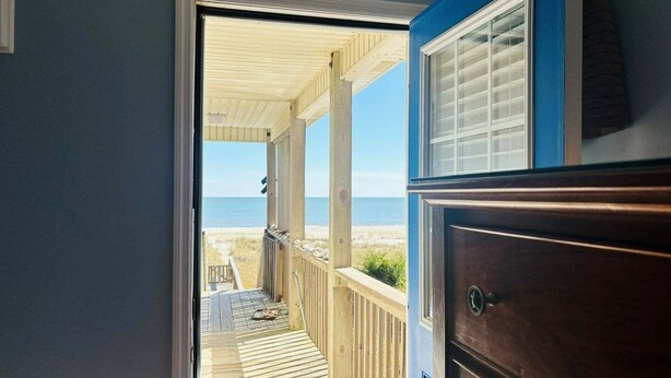Une terrasse en bois donnant sur la plage, une commode en bois foncé et un mur bleu.