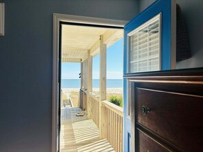 A wooden deck leading to a beach view, a dark wooden dresser, and a blue wall.