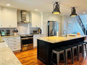 A modern kitchen with white cabinets, stainless steel appliances, a large island with bar stools, and a staircase leading to another level.