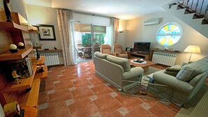 Een woonkamer met een bank, fauteuils, een televisie en een eethoek met een tafel en stoelen.