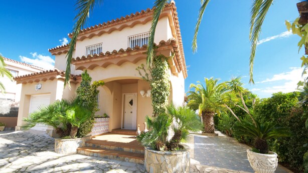 Een gebouw in mediterrane stijl met een betegeld dak, een centrale ingang met treden en bloempotten rondom de entree.