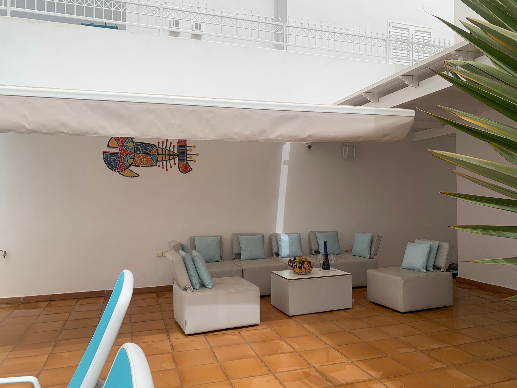 Een ruime woonkamer met een hoge nok, een decoratief muurschilderij en een trap naar een hoger gelegen verdieping.