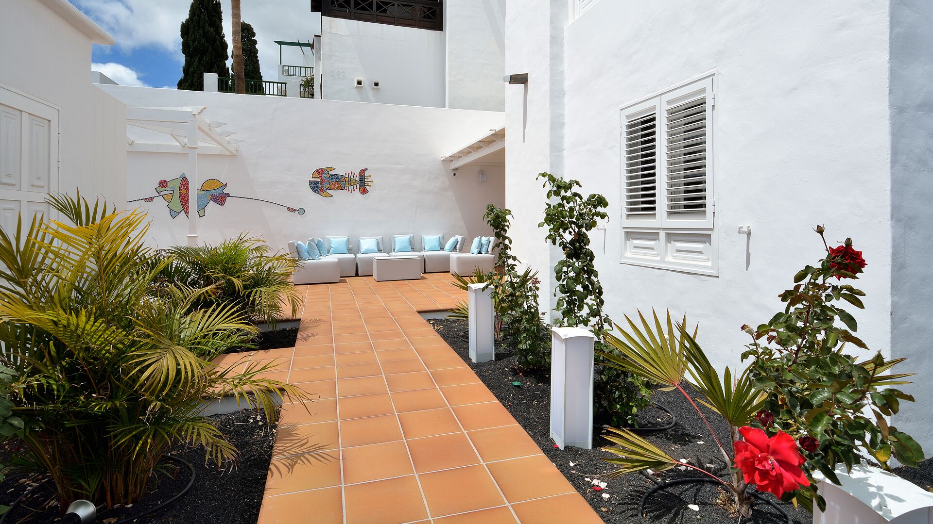 A courtyard with a tiled pathway, outdoor seating, and potted plants.