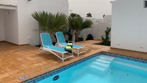 Ein Schwimmbecken mit zwei Liegestühlen, einer gefliesten Terrasse und Topfpflanzen.