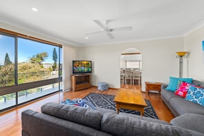 A modern living room with a large TV, a ceiling fan, and a view of the outdoors.