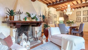 Una sala de estar acogedora con chimenea, muebles blancos y una zona de comedor con una mesa dispuesta para dos.