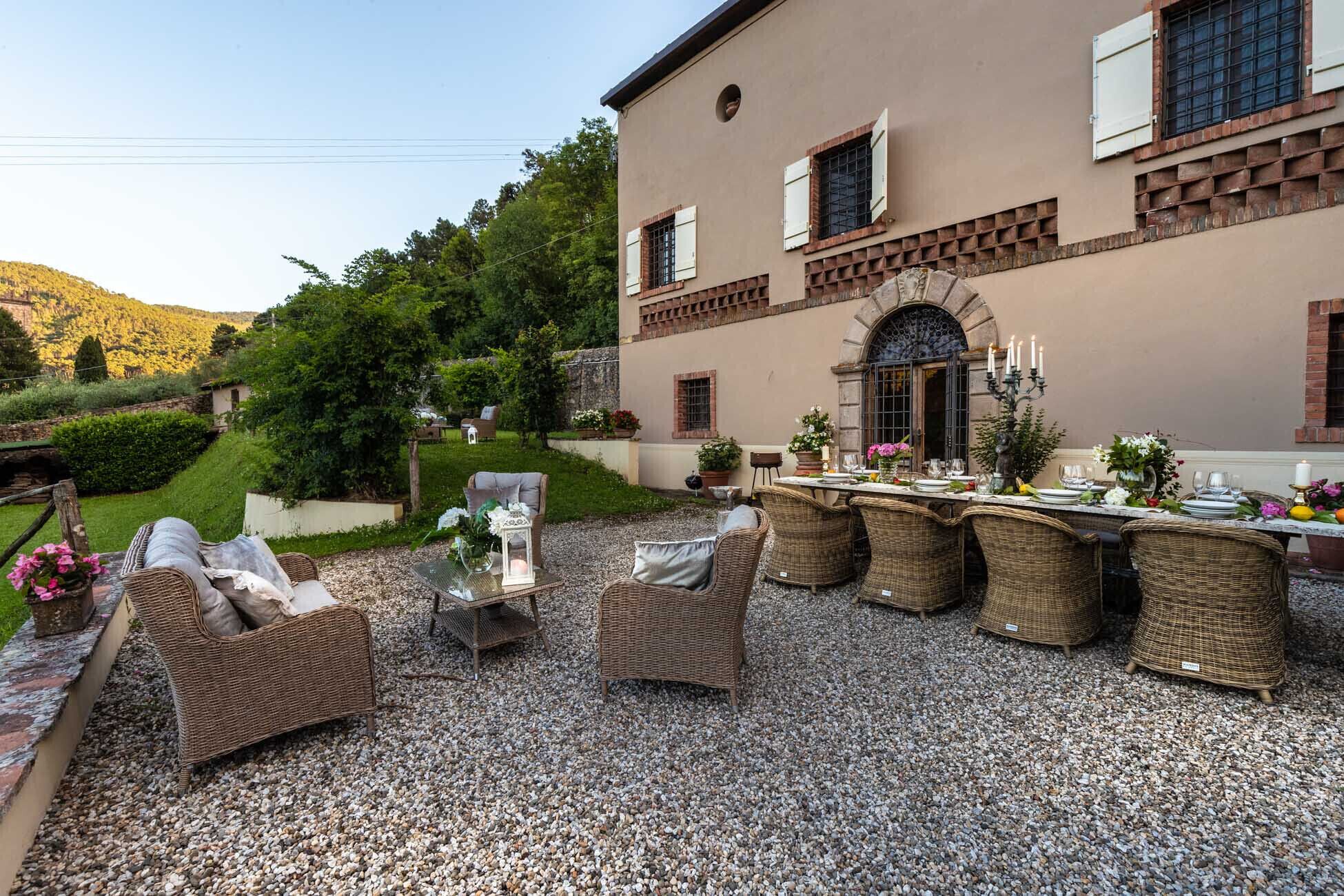 Un espace extérieur aménagé pour les repas, avec des meubles en osier et une table dressée, entouré d’une terrasse en gravier et d’un bâtiment à la façade en pierre.