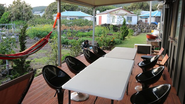 Un espacio de estar al aire libre cubierto con mesa y sillas, una hamaca y vistas a un jardín y casas.