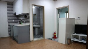 Cocina compacta con lavamanos, un refrigerador pequeño y un microondas. Hay un extintor cerca de la entrada.