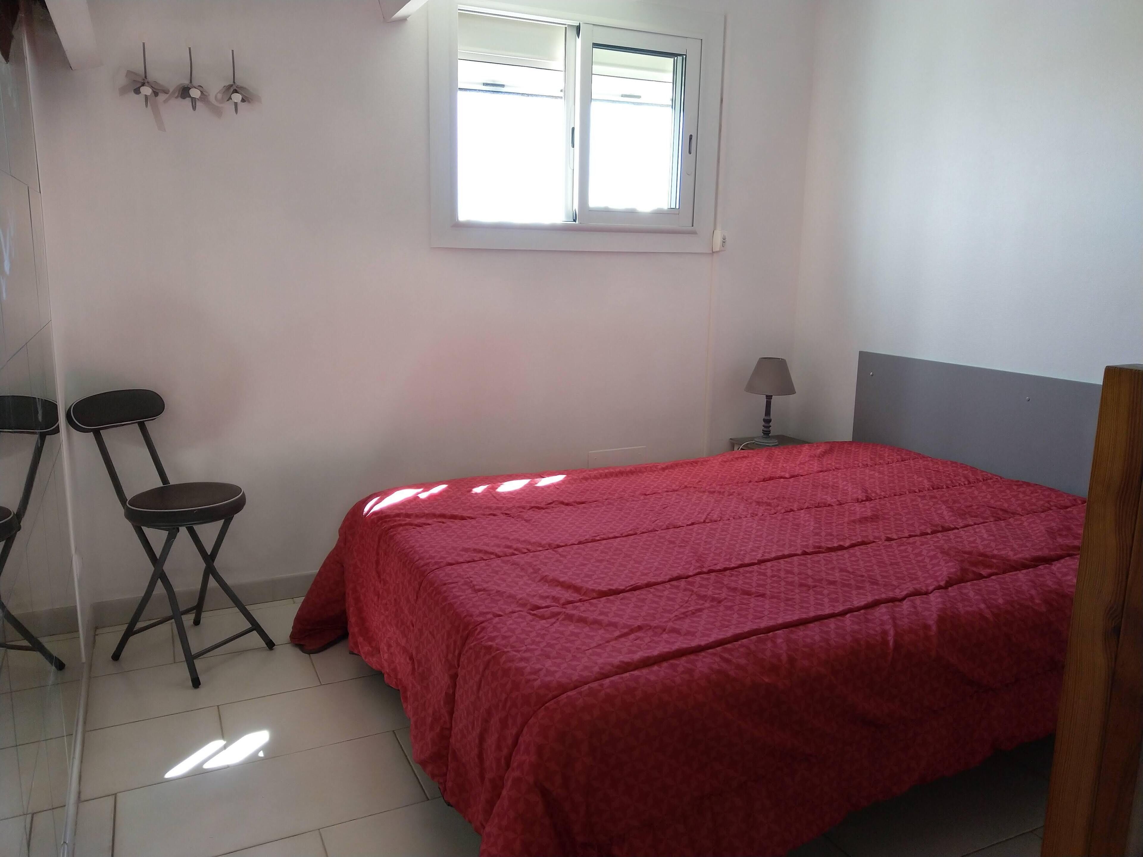 A bedroom with a bed, a window, a nightstand, and two chairs.
