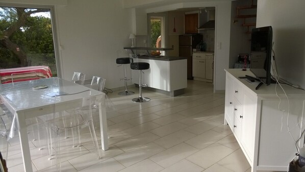 Een moderne keuken met witte kasten, een centraal eiland en een eethoek met een glazen tafel en stoelen.