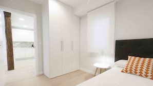 A modern bedroom with a bed, a nightstand, a wardrobe, and a view of a kitchen area. - Verona | The Rentals Collection (San Sebastián/Donostia)