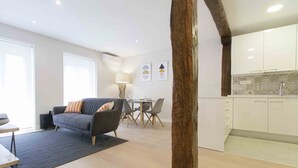 A modern living room with a grey sofa, a dining table with chairs, and a kitchen area with white cabinets. - Verona | The Rentals Collection (San Sebastián/Donostia)