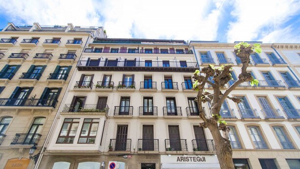A multi-story building with balconies, a tree in front, and a store named "ARISTEGUI" on the ground floor. - Verona | The Rentals Collection (San Sebastián/Donostia)
