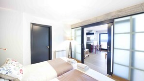 A hotel room with a bed, a desk, and a view through a sliding door. - Niza | The Rentals Collection (San Sebastián)