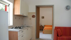 A compact kitchen with a gas stove, sink, and wooden cabinets. A red-striped sofa is visible in the adjacent living area.