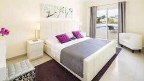 Ein Schlafzimmer mit einem Bett, Nachttischen, einem Sessel und Blick auf einen Pool.