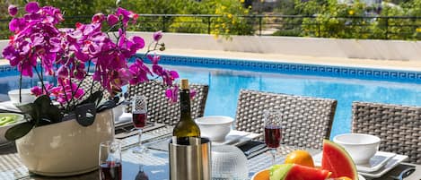 Une table dressée pour le dîner, avec vue sur une piscine et une végétation luxuriante en arrière-plan.