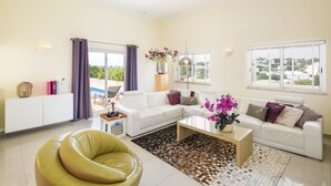 Ein modernes Wohnzimmer mit einem weißen Sofa, einem gelben Sessel, einem Couchtisch und Blick ins Freie durch große Fenster.