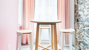 Un coin repas avec une table ronde et trois tabourets, des rideaux roses et un mur en pierre.