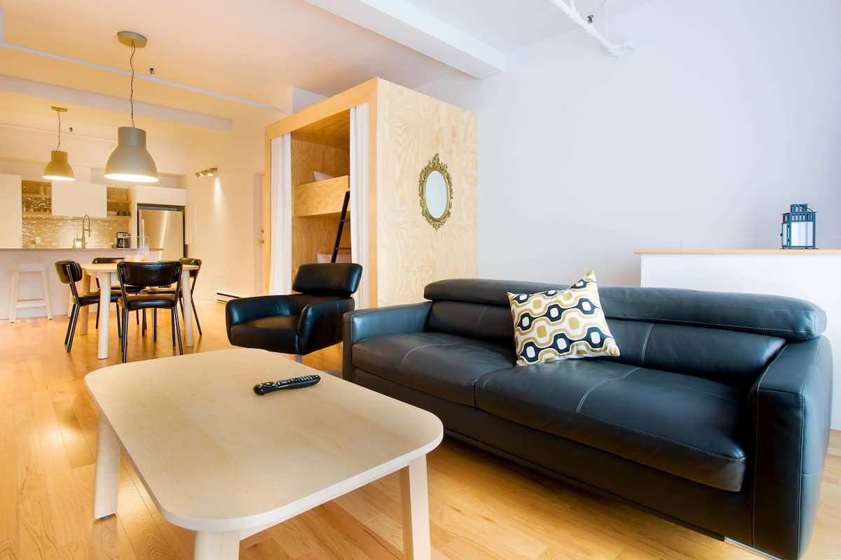 Un salon moderne avec un canapé en cuir noir, une table basse blanche et un coin repas comprenant des chaises et une table.