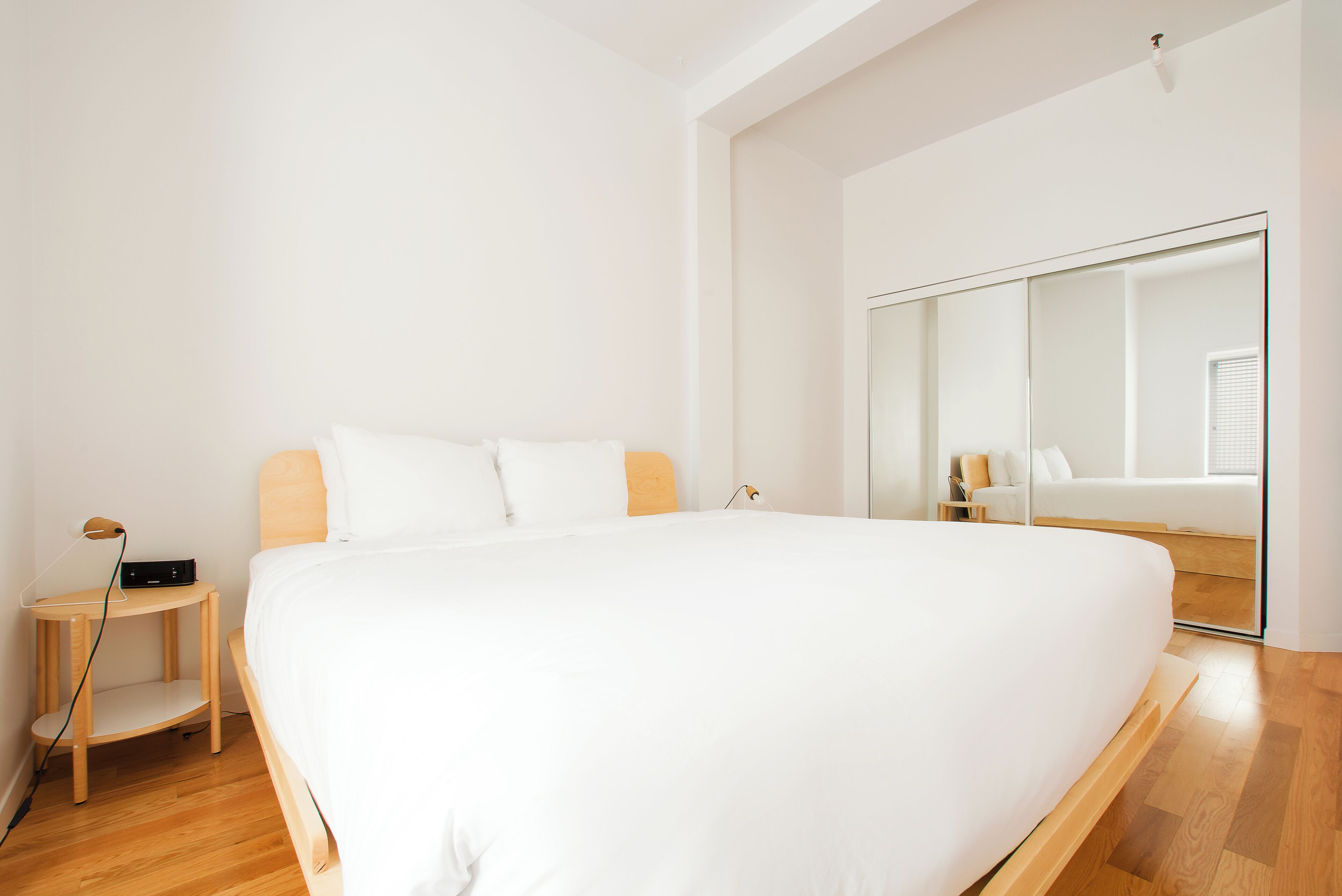 Een groot bed met houten hoofdbord, nachtkastje met lamp en spiegel aan de muur.