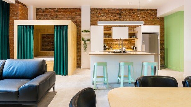 Un salon moderne comprenant un canapé, une table à manger et un coin cuisine avec un mur en briques et des touches de vert.