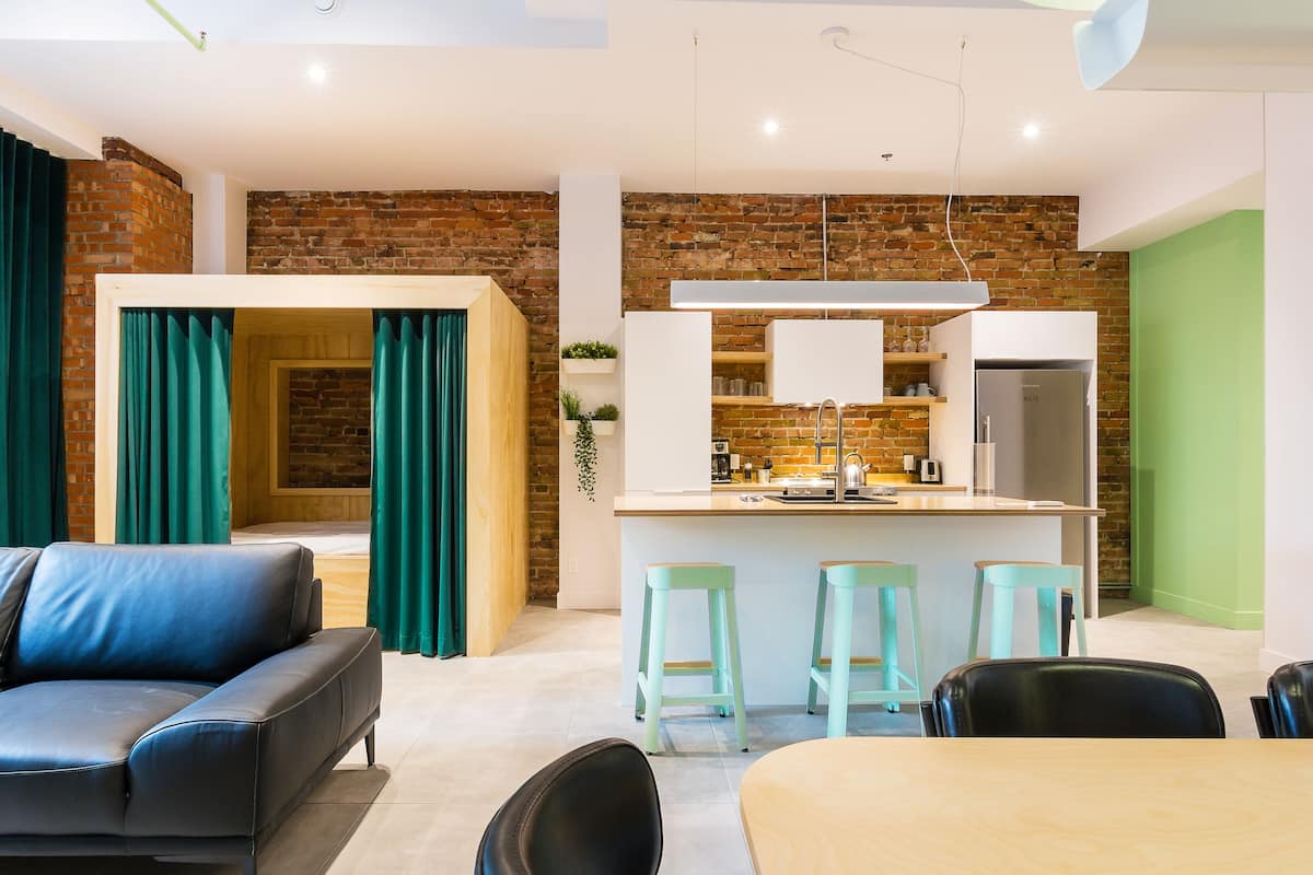 Un salon moderne comprenant un canapé, une table à manger et un coin cuisine avec un mur en briques et des touches de vert.
