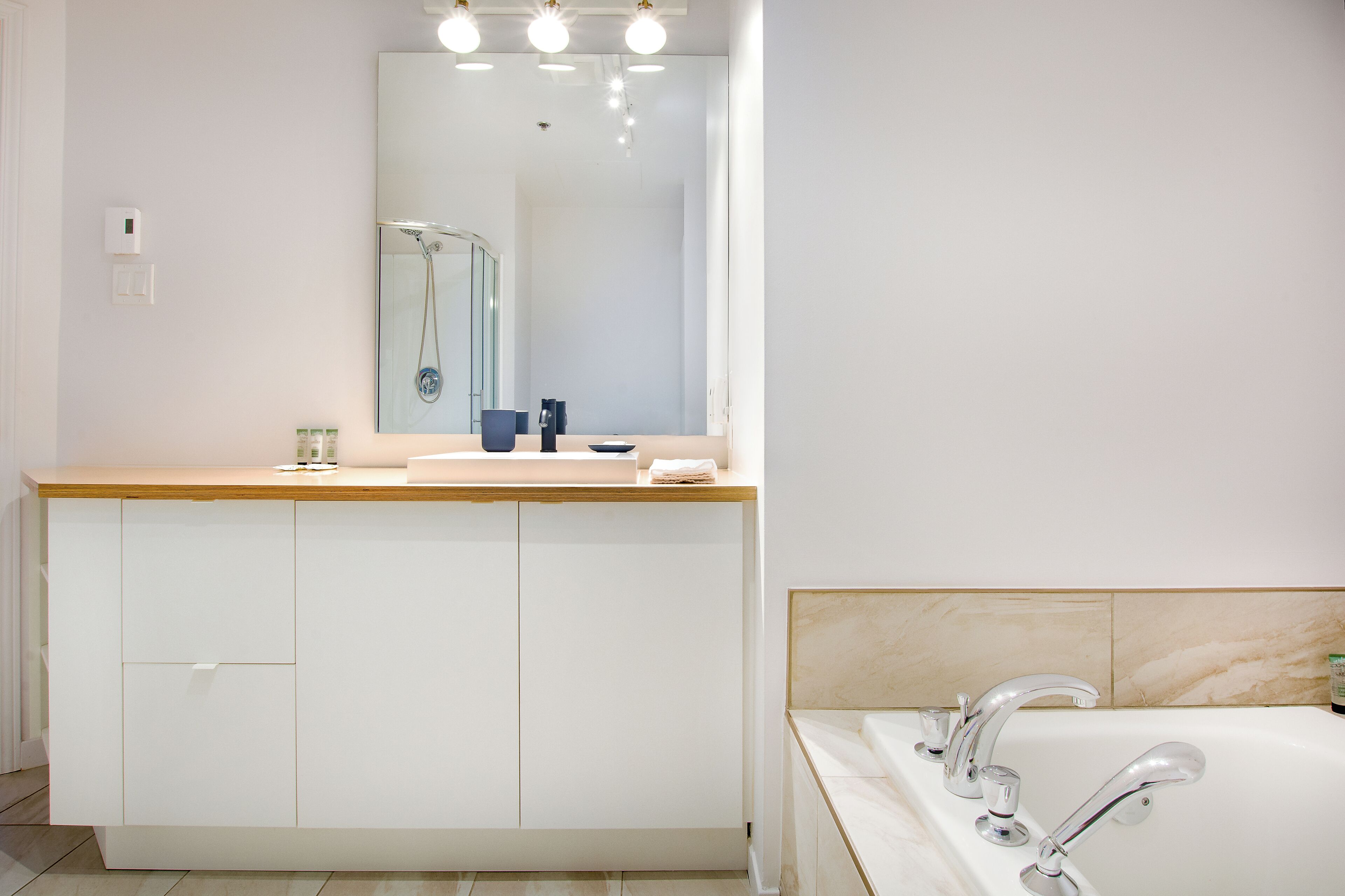 Une salle de bain moderne avec un meuble-lavabo en bois, un grand miroir, une baignoire et une douche.