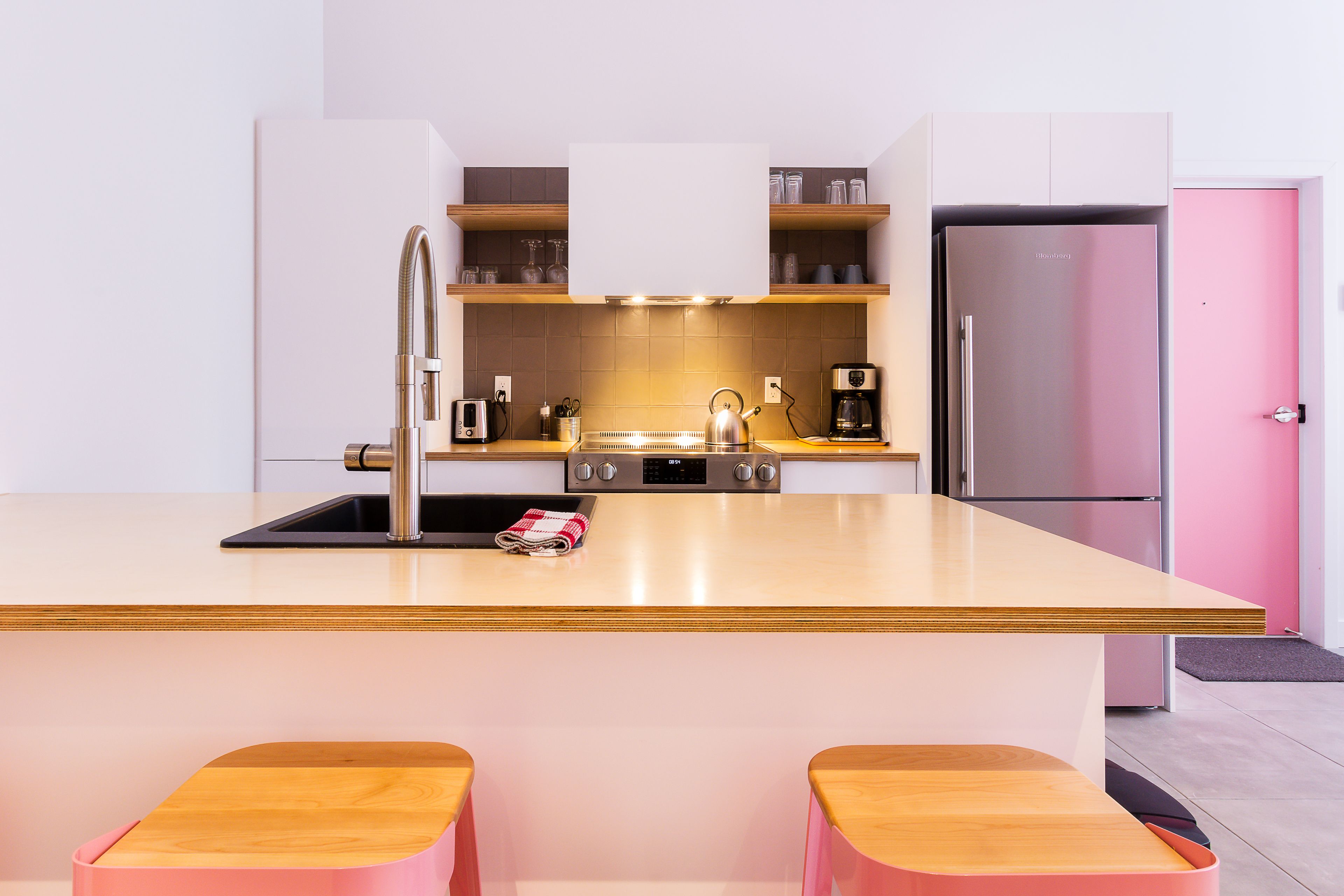 A modern kitchen with a central island, stainless steel appliances, and a pink refrigerator.