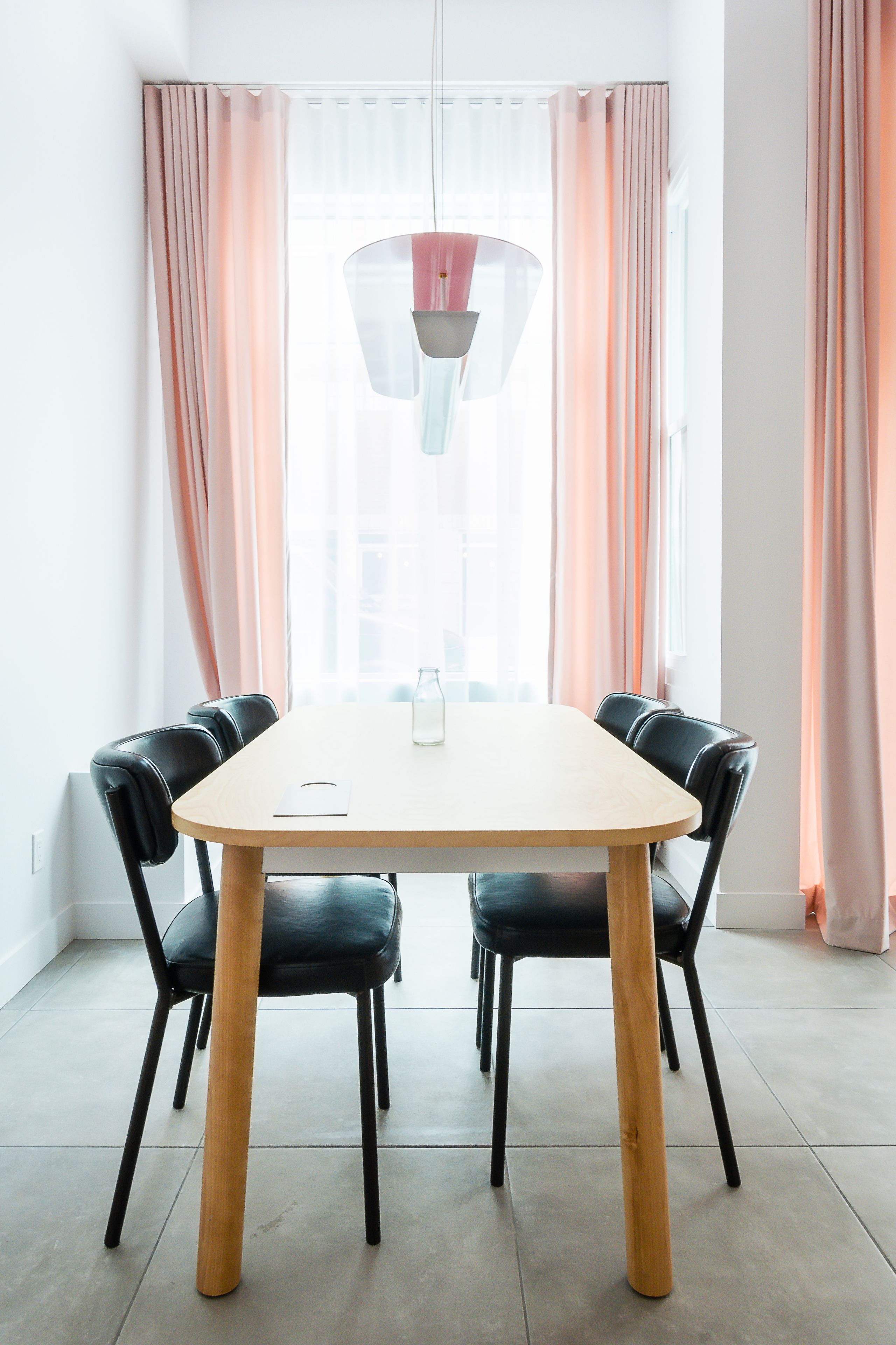 Un coin repas avec une table et des chaises, une bouteille posée sur la table et des rideaux aux fenêtres.