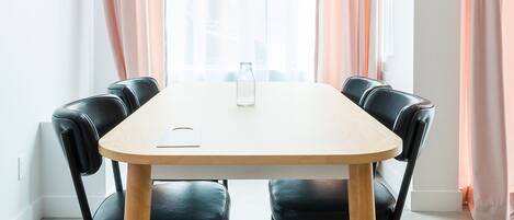 Un coin repas avec une table et des chaises, une bouteille posée sur la table et des rideaux aux fenêtres.