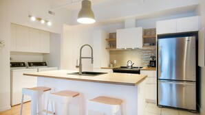 Une cuisine moderne avec des meubles blancs, un réfrigérateur en acier inoxydable, un évier et trois tabourets de bar.
