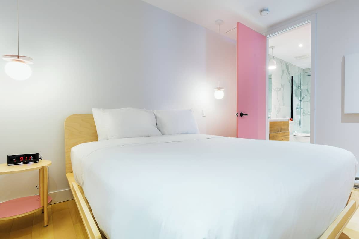 Une chambre à coucher moderne avec un grand lit, une table de chevet et une porte rose donnant accès à une salle de bain.