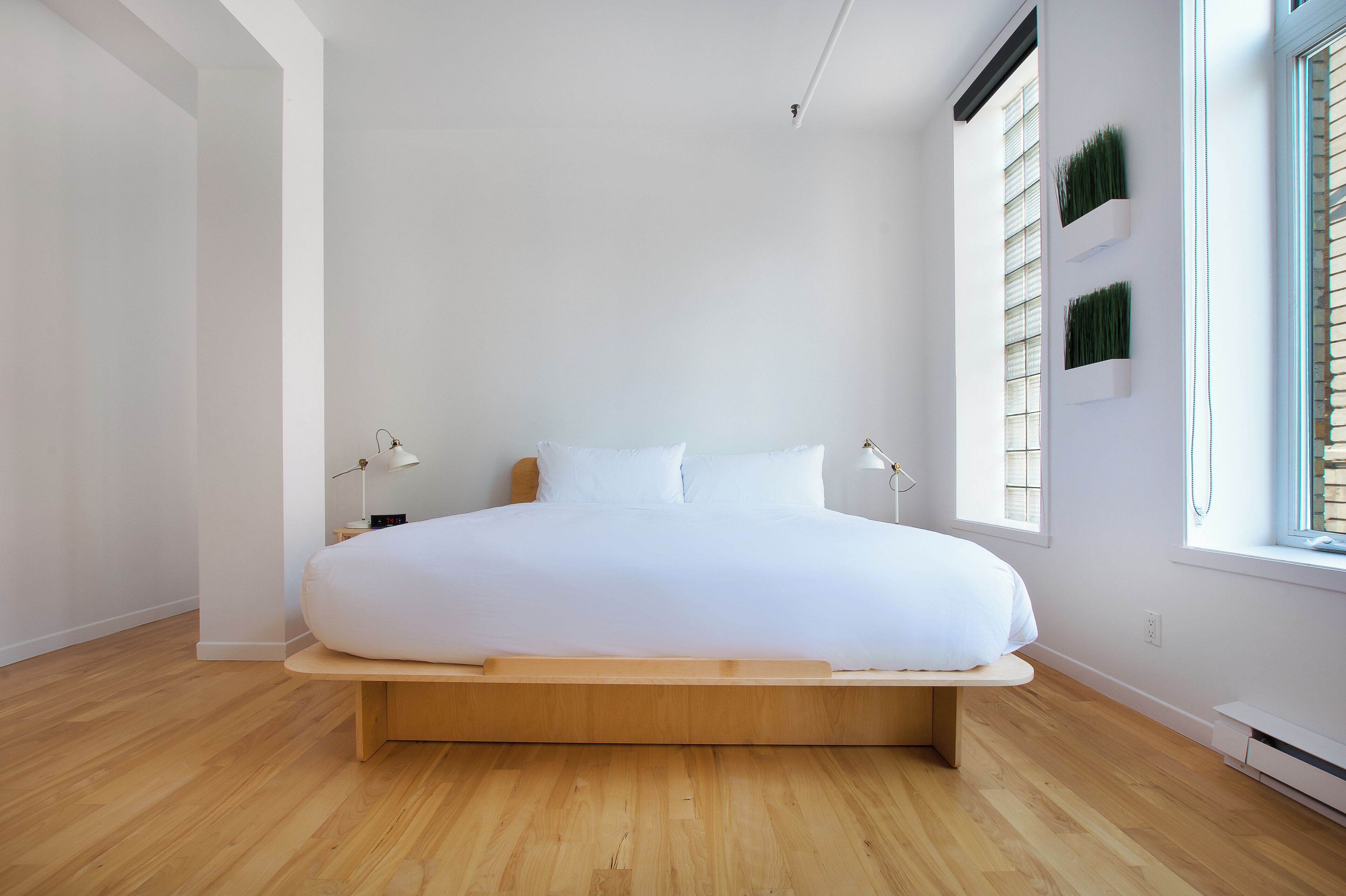 Un dormitorio minimalista con una cama grande, paredes blancas y suelo de madera.