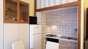 A compact kitchen with a refrigerator, stove, and a microwave on top. There is a dining table with chairs and a cabinet with glass doors. - Eveten 1 - apartment for 4, in town centre, 500 metres from the beach, with parking (Diano Marina)
